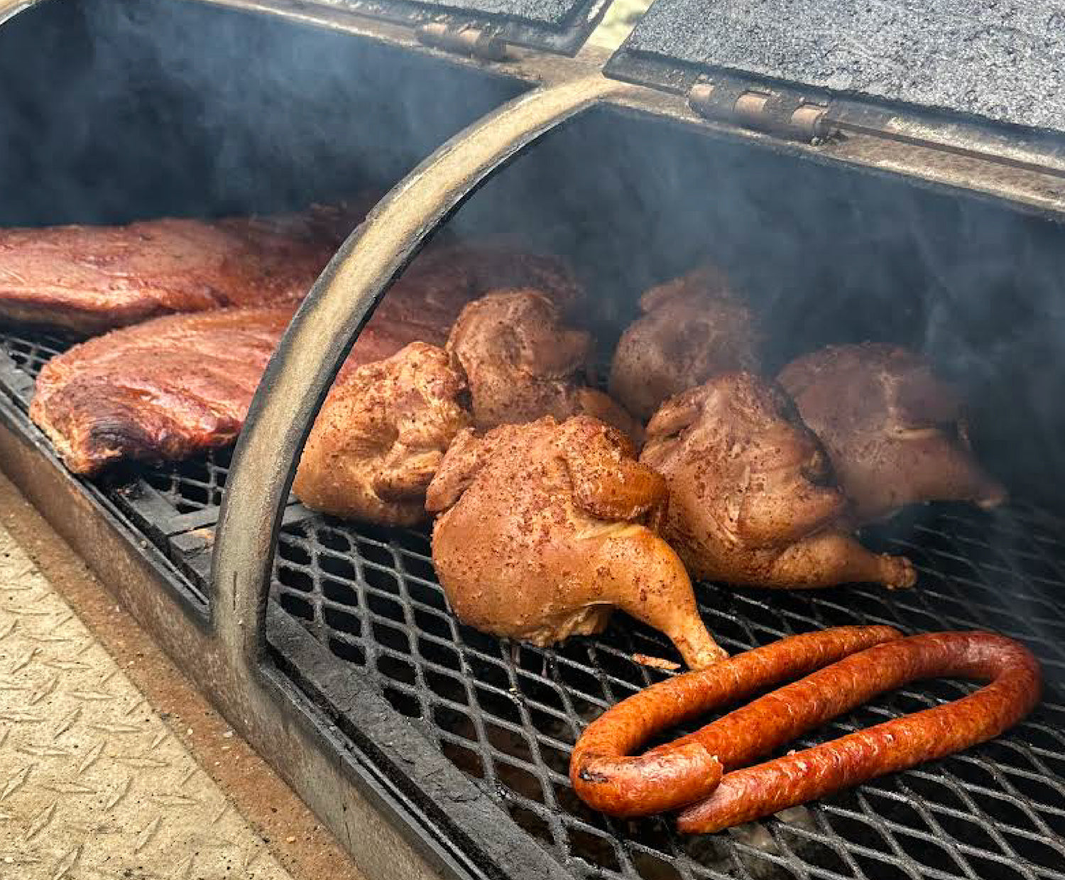 A smoker containing ribs, whole chickens, and sausage
